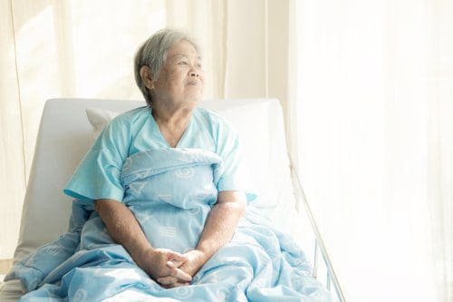 Elderly man wearing a protective face mask looks out of a window.